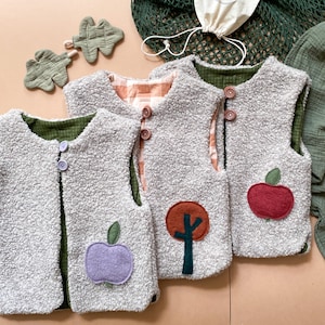 Könnte beinhalten: Drei ärmellose Westen aus grauem, strukturiertem Fleece-Material. Jede Weste verfügt über eine Knopfleiste vorne und eine einzigartige Filzapplikation: einen lila Apfel, einen braunen Baum und einen roten Apfel. Gefüttert mit grünem oder orangefarbenem Karostoff.