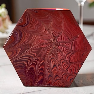 May include: A hexagonal decorative object with a swirling pattern in shades of red, burgundy, and brown. The object has a glossy finish and is likely made of resin or a similar material. The design resembles a marbled effect.