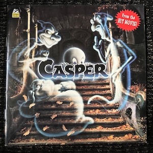 以下が含まれることがあります： 映画「キャスパー」のフレンドリーな幽霊、キャスパーをフィーチャーした本の表紙。表紙は黒で、キャスパーと他の3人の幽霊の漫画画像が描かれている。「キャスパー」という文字は大きな白い文字で、「From the HIT MOVIE!」という文字は白い星の上に赤い文字で書かれている。
