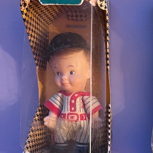 May include: A vintage plastic doll in a baseball uniform, packaged in a box with the text "Heewees" Tiny He-Men of the Pee Wee World" and "Uneeda Doll Co., Inc. 1966".