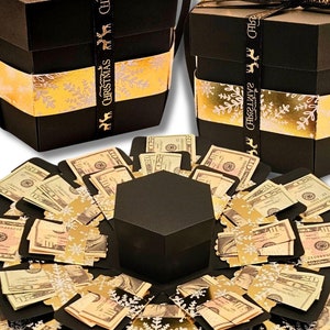 May include: Two black hexagonal gift boxes with gold snowflake accents and Christmas ribbon. One box is open, revealing a display of folded money. The text "MONEY NOT INCLUDED" is at the bottom.