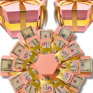 May include: Pink hexagonal explosion box with gold ribbon and dollar bills inside.  The box is open and the dollar bills are visible.  The text "MONEY NOT INCLUDED" is printed below the box.
