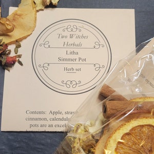 May include: A herb set for simmering, featuring dried orange slices, cinnamon sticks, and other botanicals. The set includes a card with the text "Two Witches Herbals, Litha Simmer Pot, Herb set". The package is labeled "Compostable".