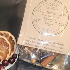 May include: A New Year's Eve Simmer Pot herb set from Two Witches Herbals. The set includes apple, lemon, cranberry, cinnamon, peppermint, fennel, sage, and rosemary. Dried orange slices and berries are on a small plate.