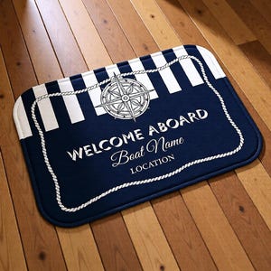 May include: A rectangular navy blue welcome mat with white stripes and a nautical compass design. The mat has the words "WELCOME ABOARD" and space for "Boat Name" and "LOCATION" in white script, framed by a white rope border.