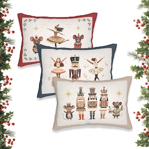 Könnte beinhalten: Drei rechteckige dekorative Kissen mit festlichen Illustrationen. Die Kissen zeigen Bilder von Mäusen, Ballerinas und Nussknackern in einem skurrilen Stil. Jedes Kissen hat einen unterschiedlich farbigen Rand: rot, marineblau und beige.