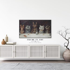 May include: A framed print of a vintage illustration featuring five cats sitting at a bar, with one cat holding a glass of beer. The print is hanging on a white wall above a white cabinet with woven rattan doors. A vase with a dried branch arrangement is on the right side of the cabinet.