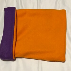 May include: A small, rectangular fleece sleep sack for a pet. It is orange with a purple trim.