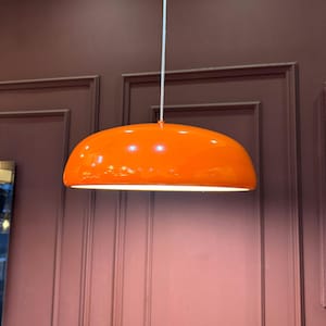May include: A bright orange pendant light fixture hangs from the ceiling. The light fixture is shaped like a dome and has a white cord.