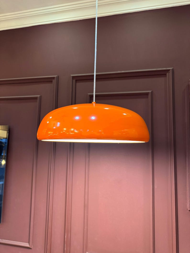 May include: A bright orange pendant light fixture hangs from the ceiling. The light fixture is shaped like a dome and has a white cord.