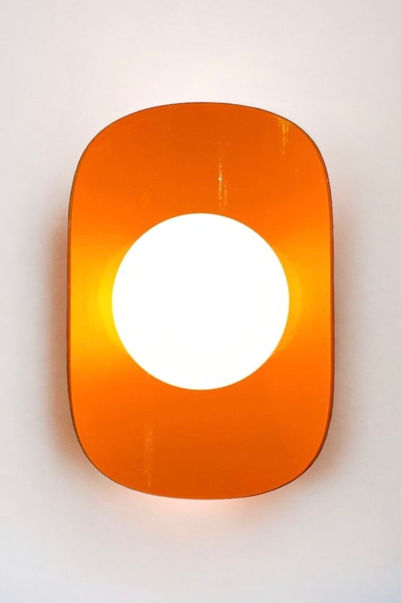 May include: Orange wall sconce with a round white light in the center.