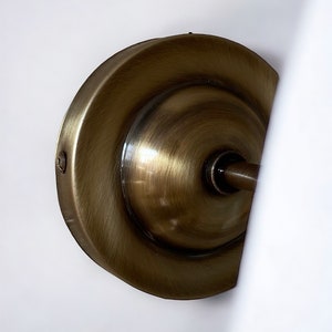 May include: A close-up of a brass wall sconce with a round, decorative backplate. The sconce has a smooth, polished finish and a slightly curved design.