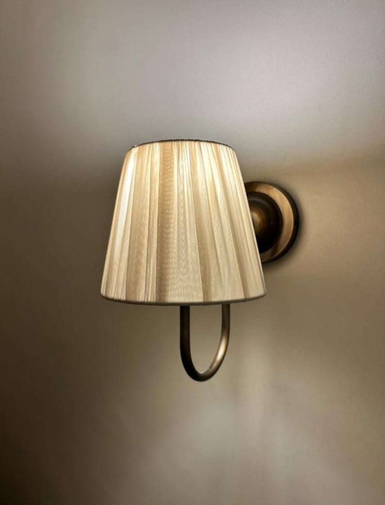 May include: A wall-mounted light fitting with a cream-coloured pleated fabric shade and a gold-toned metal base.