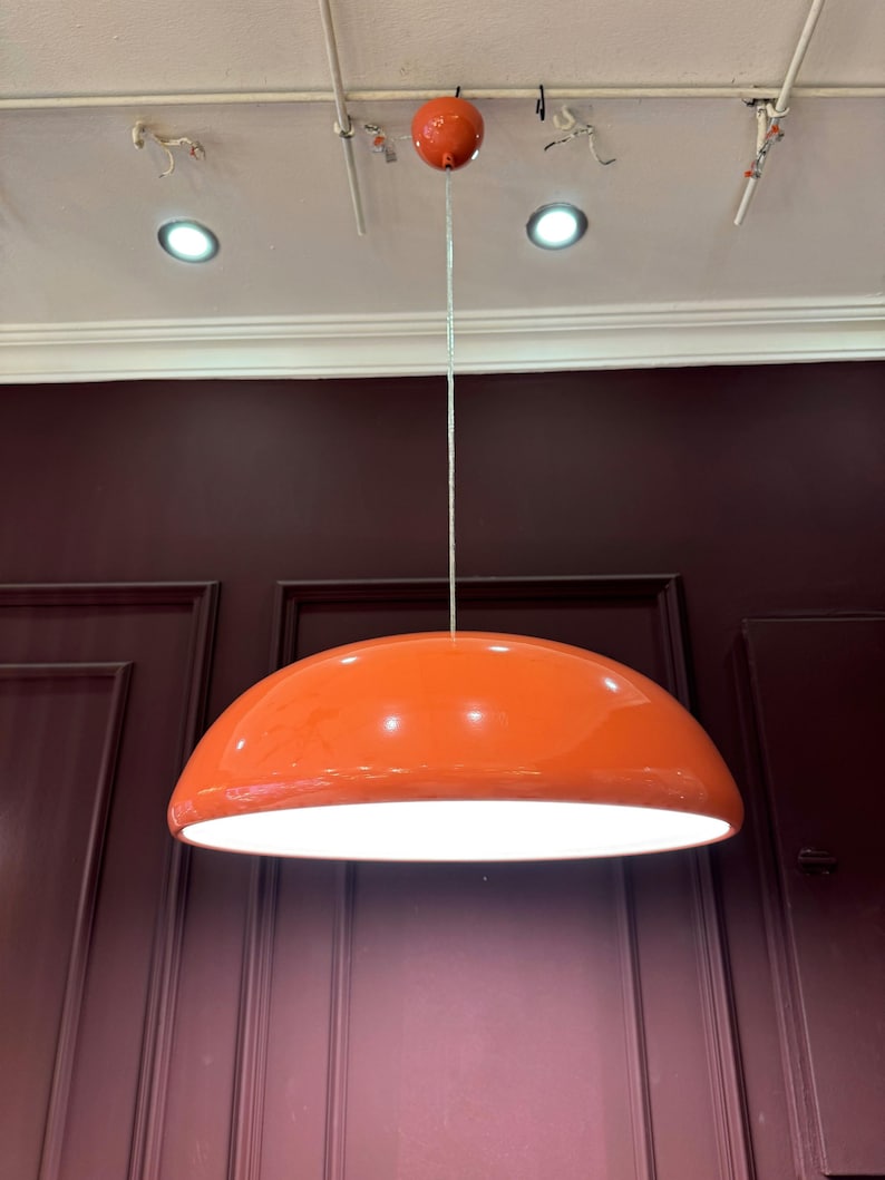 May include: A large, orange, dome-shaped pendant light fixture hangs from the ceiling. The light fixture is made of a smooth, glossy material and has a white interior.
