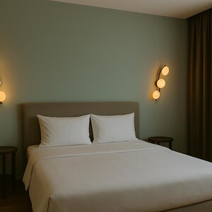 May include: A bedroom scene featuring a bed with white linens and pillows. Two small wooden side tables flank the bed. The walls are a muted green, with decorative wall sconces on either side of the bed, each with three glowing orbs.