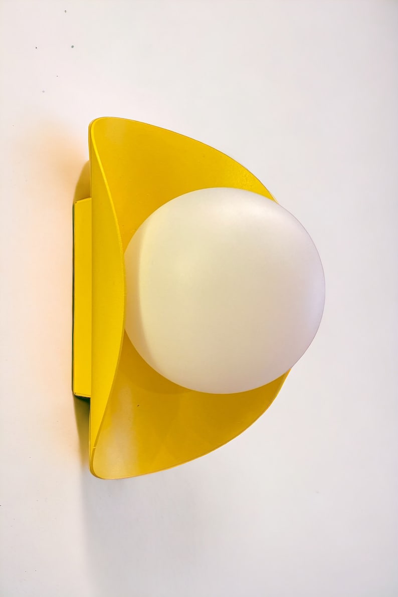 May include: A yellow wall sconce with a white globe light fixture. The sconce is shaped like a crescent moon.