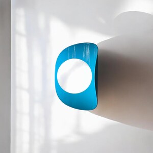 May include: A blue and white wall sculpture with a circular opening. The sculpture is mounted on a white wall.