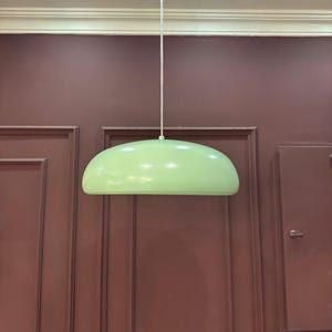May include: A light green pendant lamp hanging from the ceiling against a maroon wall.