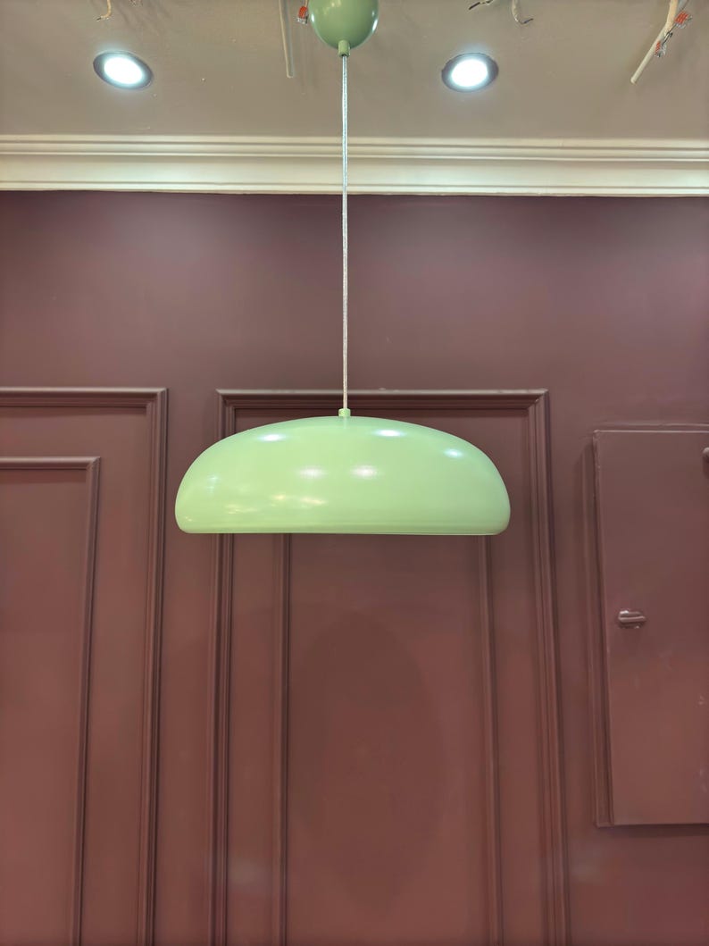May include: A light green pendant lamp hanging from the ceiling against a maroon wall.