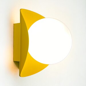 May include: A yellow wall sconce with a white globe light fixture. The sconce has a curved, geometric design.
