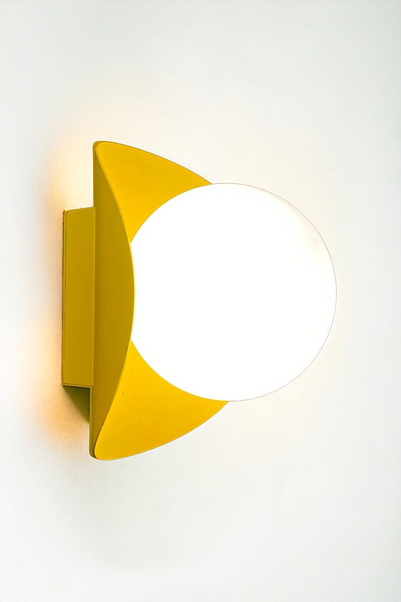 May include: A yellow wall sconce with a white globe light fixture. The sconce has a curved, geometric design.
