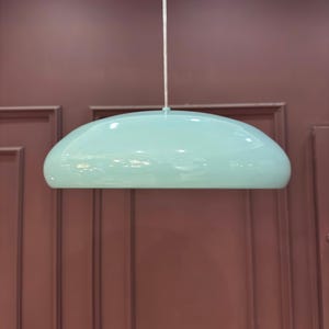 May include: A light blue, dome-shaped pendant light fixture hangs from a white cord against a maroon wall.