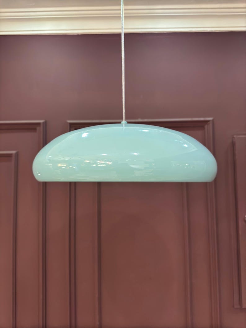 May include: A light blue, dome-shaped pendant light fixture hangs from a white cord against a maroon wall.