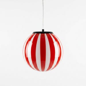 May include: A red and white striped pendant light fixture. The spherical lamp has vertical stripes and a black cap. The light hangs from a thin wire against a white background. The lamp is a decorative lighting element.