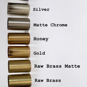 May include: A close-up of eight metal cylinders in different finishes, from left to right: platinum, silver, matte chrome, honey, gold, raw brass matte, raw brass, and antique brass.