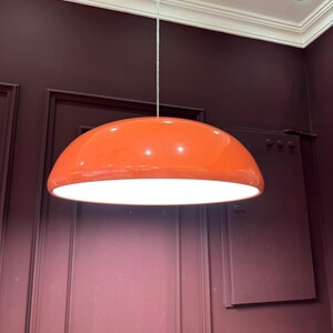 May include: A bright orange pendant light fixture with a white interior, hanging from a white ceiling.