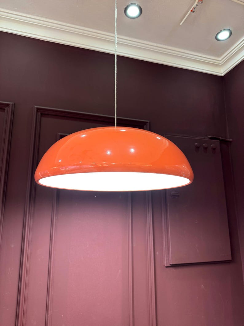 May include: A bright orange pendant light fixture with a white interior, hanging from a white ceiling.
