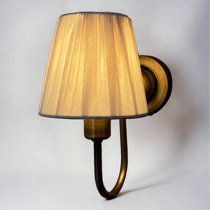 May include: A gold wall sconce with a pleated fabric lampshade. The lampshade is a light beige colour.