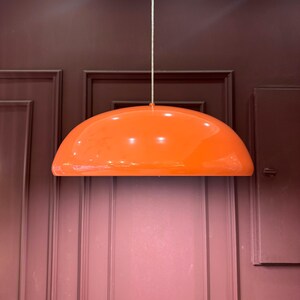 May include: A bright orange, dome-shaped pendant light fixture hangs from a white ceiling against a burgundy wall.