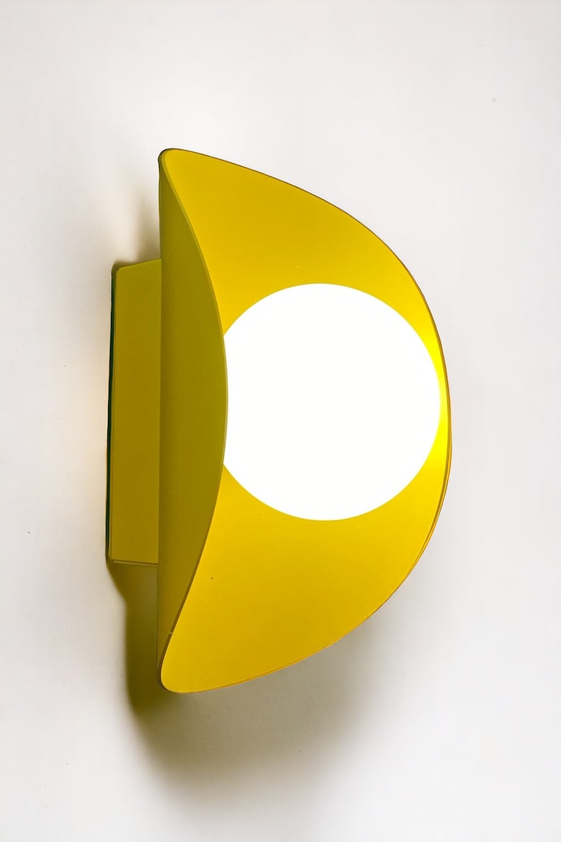 May include: A yellow wall sconce with a circular light fixture. The sconce is shaped like a crescent moon.