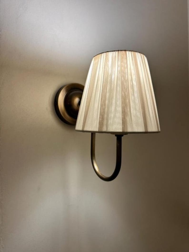 May include: A brass wall sconce with a pleated off-white fabric lampshade.