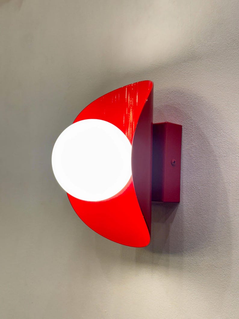 May include: A red and burgundy wall sconce with a white globe light bulb. The sconce is shaped like a crescent moon.