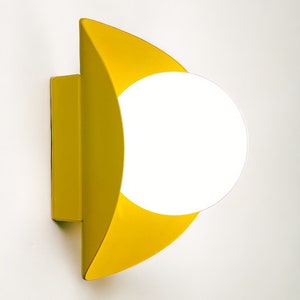 May include: A yellow wall sconce with a white globe light fixture. The sconce is shaped like a crescent moon.