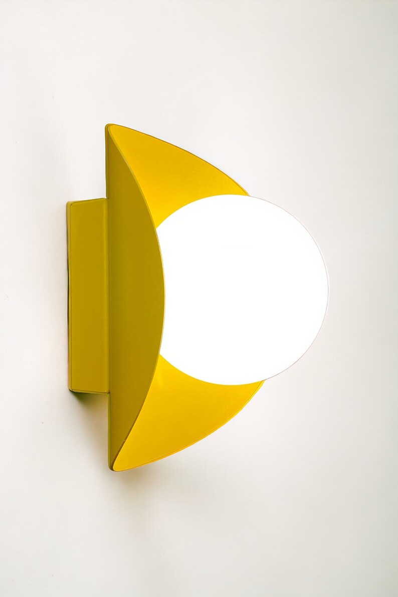 May include: A yellow wall sconce with a white globe light fixture. The sconce is shaped like a crescent moon.