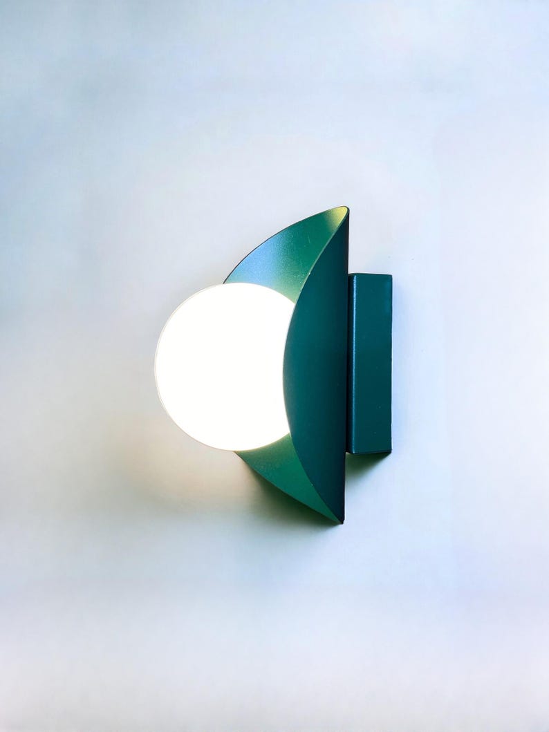 May include: A teal green wall sconce with a white globe light fixture. The sconce is shaped like a crescent moon.