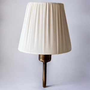 May include: A white pleated lampshade with a brass wall sconce.