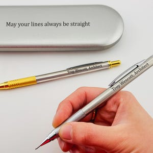 May include: Two silver mechanical pencils with gold accents. The pencils are engraved with the text "Troy Wescott, Architect". One pencil is in a silver case with the text "May your lines always be straight".