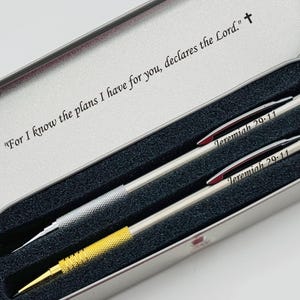 May include: A silver pen set in a metal case. The pens are silver and gold with the text "Jeremiah 29:11". The case has the text "For I know the plans I have for you, declares the Lord."