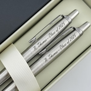 May include: Two silver pens in a white box with the inscription "R. Thomas - Class of 2025" on each pen.