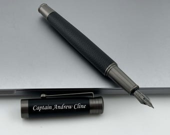 May include: A black and silver fountain pen with a textured grip and a fine nib. The pen is engraved with the name "Captain Andrew Cline".