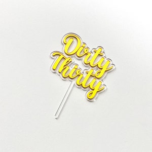 May include: A yellow acrylic cake topper with the words "Dirty Thirty" in a cursive font.