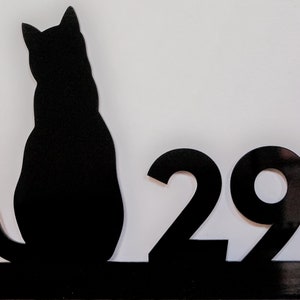 May include: Black silhouette of a cat sitting on a black metal base with the number 29 on the right side.