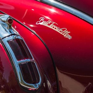 May include: Close-up of a classic car's red body with chrome accents. The image highlights the car's tail light and the text "Bull Terrier Moms" in a cursive font. The car's paint has a glossy finish.