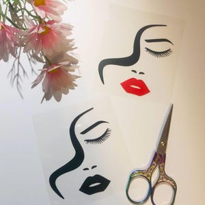 May include: Two black and white silhouette face decals with closed eyes and lips. The top decal has red lips and the bottom decal has black lips. The decals are on a white background with a pair of rainbow-colored scissors.