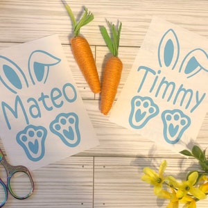 May include: Two white sheets of paper with blue bunny ears and paw prints. The names Mateo and Timmy are written on the sheets.
