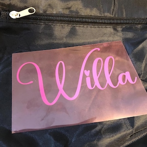 May include: Pink vinyl sticker with the name "Willa" in a cursive font with a small heart in the middle of the "i".